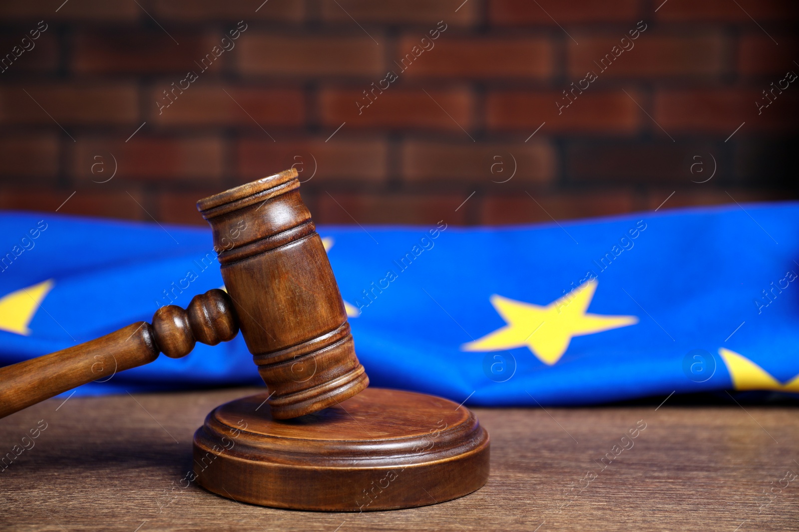 Photo of Judge's gavel and European Union flag on wooden table against brick wall, closeup. Space for text