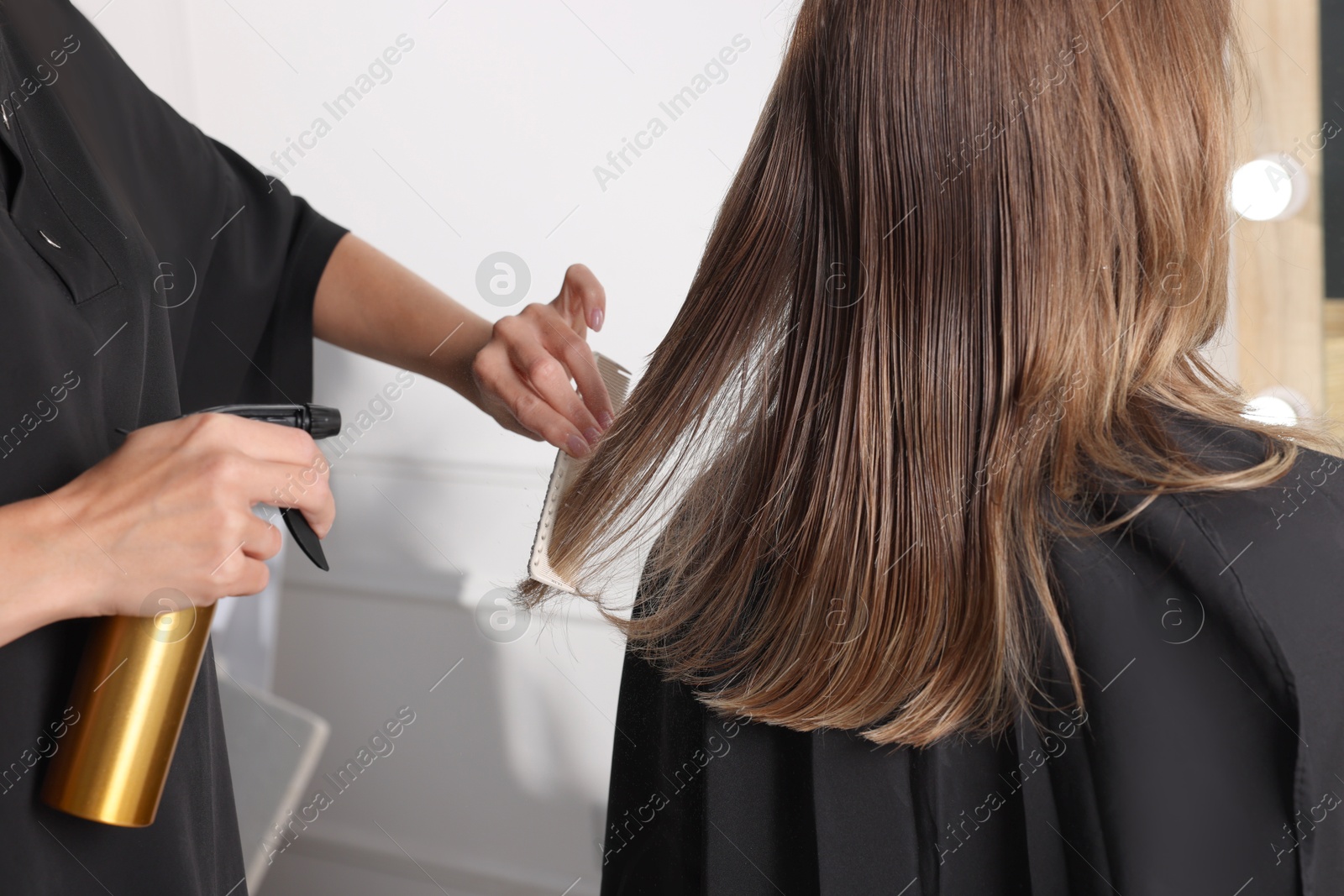 Photo of Hairdresser using spray while making stylish haircut in salon, closeup