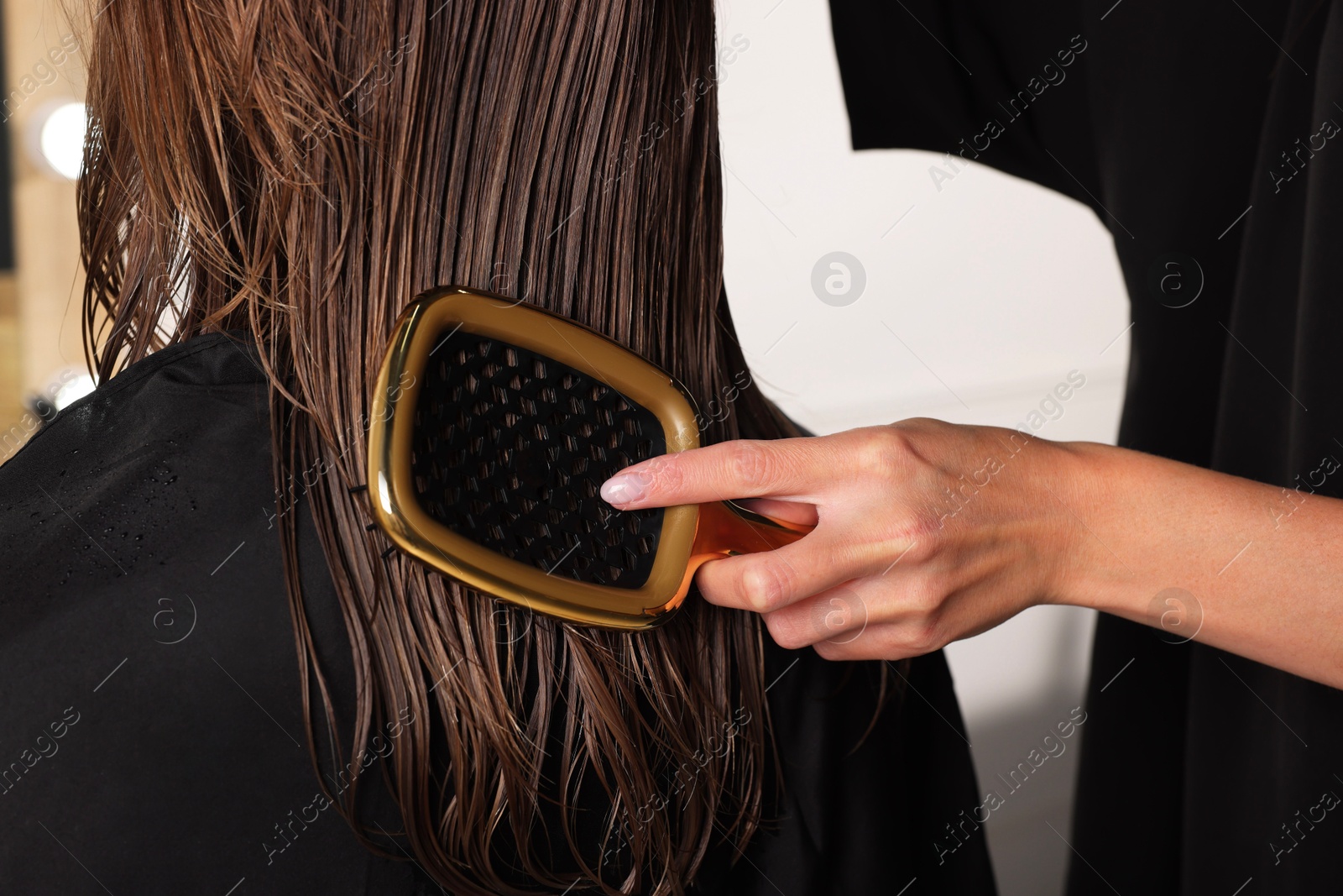 Photo of Hairdresser brushing client's wet hair in salon, closeup