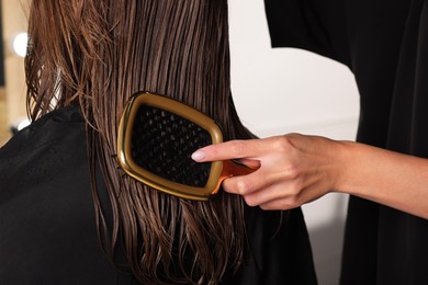 Photo of Hairdresser brushing client's wet hair in salon, closeup