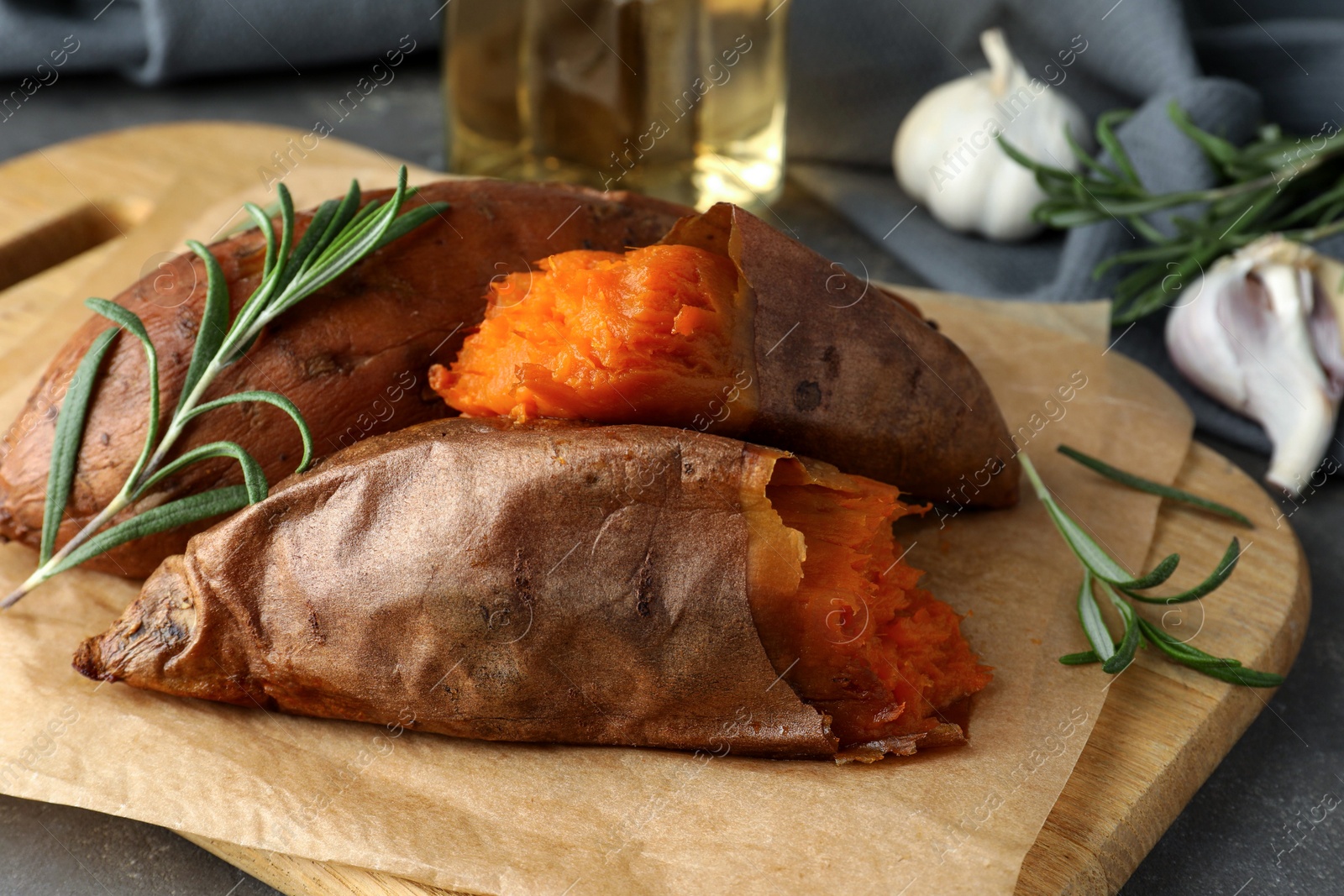 Photo of Tasty cooked sweet potatoes served with rosemary on grey table, closeup