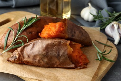 Tasty cooked sweet potatoes served with rosemary on grey table, closeup