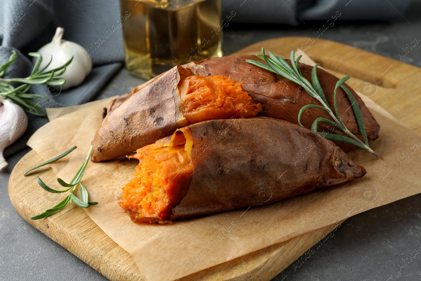 Photo of Tasty cooked sweet potatoes served with rosemary on grey table