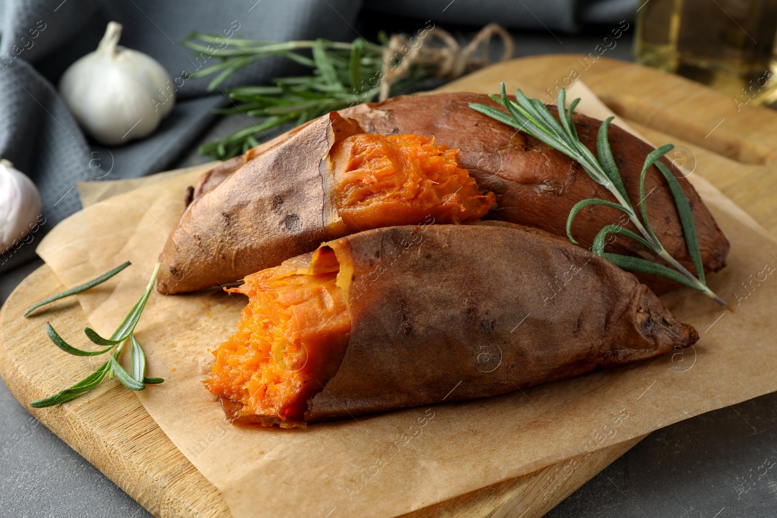 Photo of Tasty cooked sweet potatoes served with rosemary on grey table, closeup