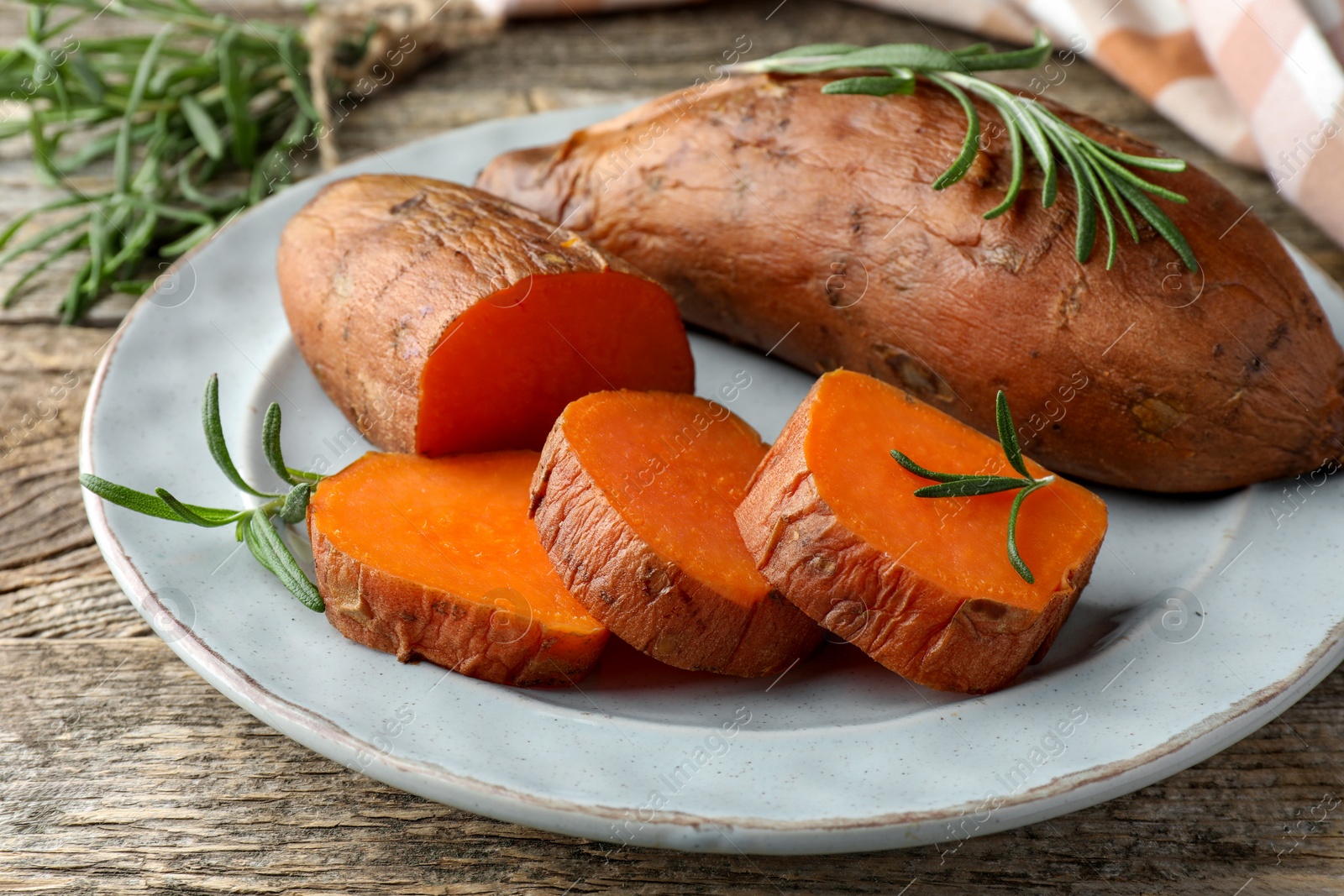 Photo of Tasty cooked sweet potatoes served with rosemary on wooden table, closeup