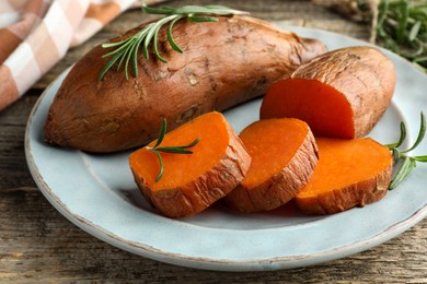 Photo of Tasty cooked sweet potatoes served with rosemary on wooden table, closeup