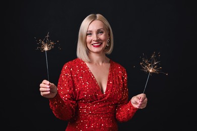 Photo of Smiling woman with sparklers celebrating Christmas on black background