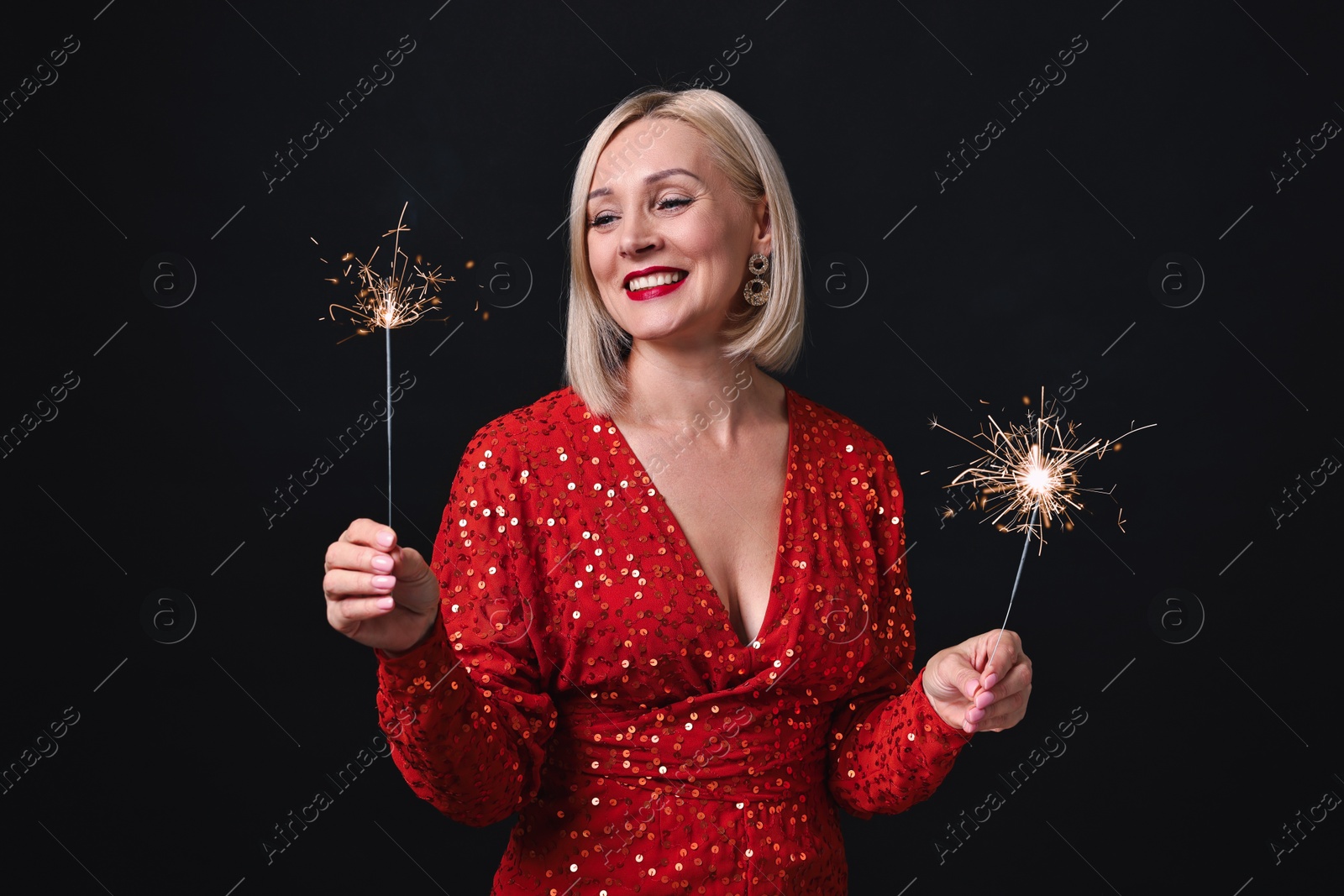 Photo of Smiling woman with sparklers celebrating Christmas on black background