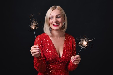 Photo of Smiling woman with sparklers celebrating Christmas on black background