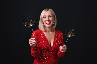 Photo of Smiling woman with sparklers celebrating Christmas on black background