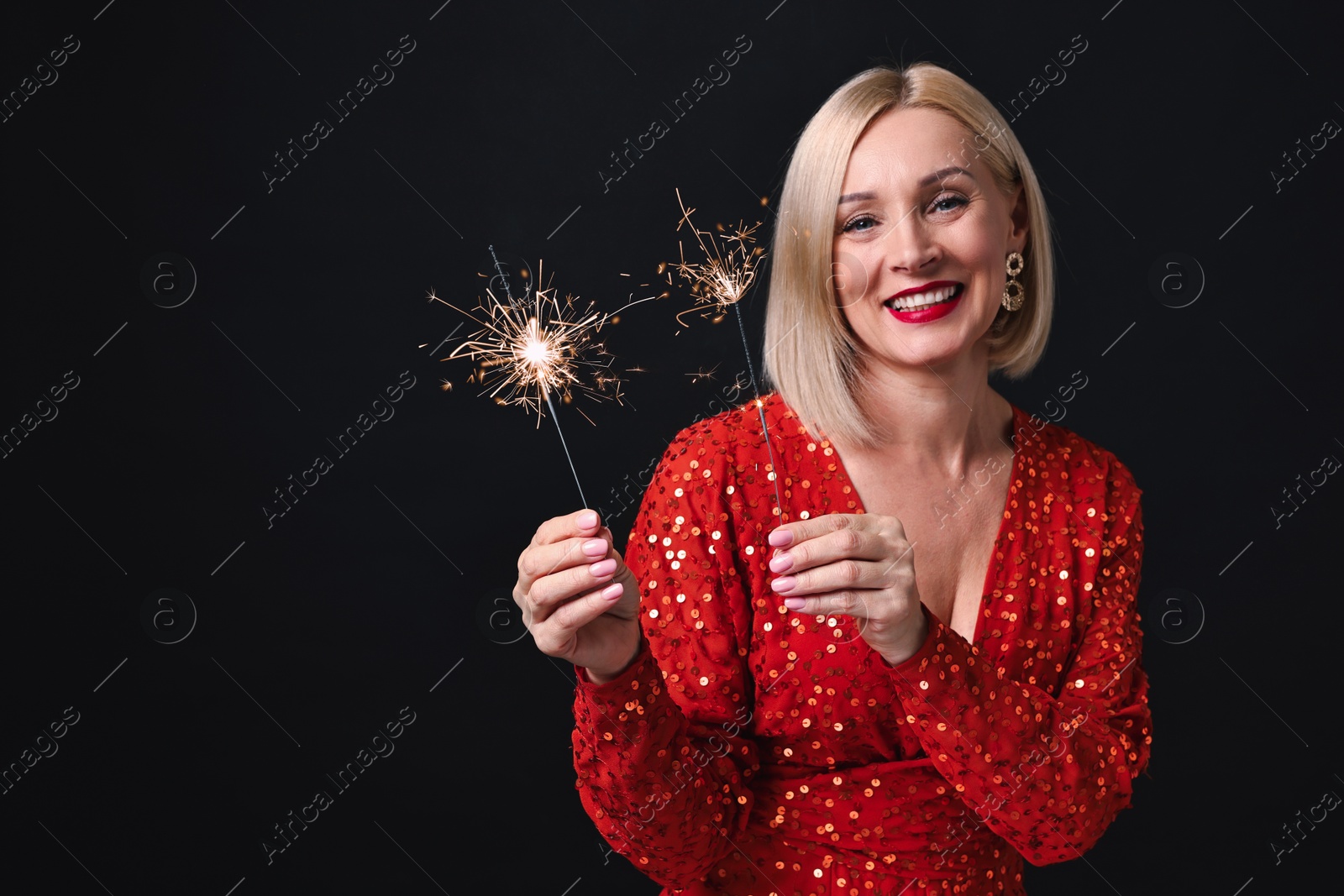 Photo of Smiling woman with sparklers celebrating Christmas on black background. Space for text