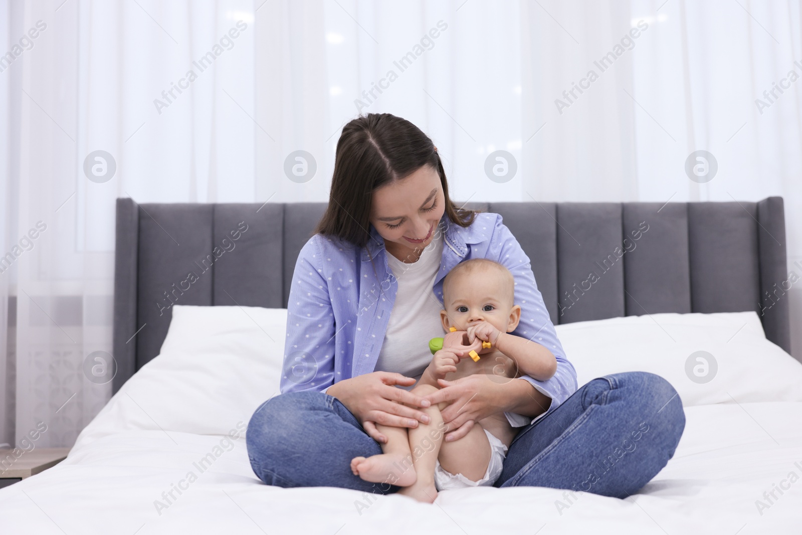 Photo of Mother and her cute little baby with rattle on bed indoors