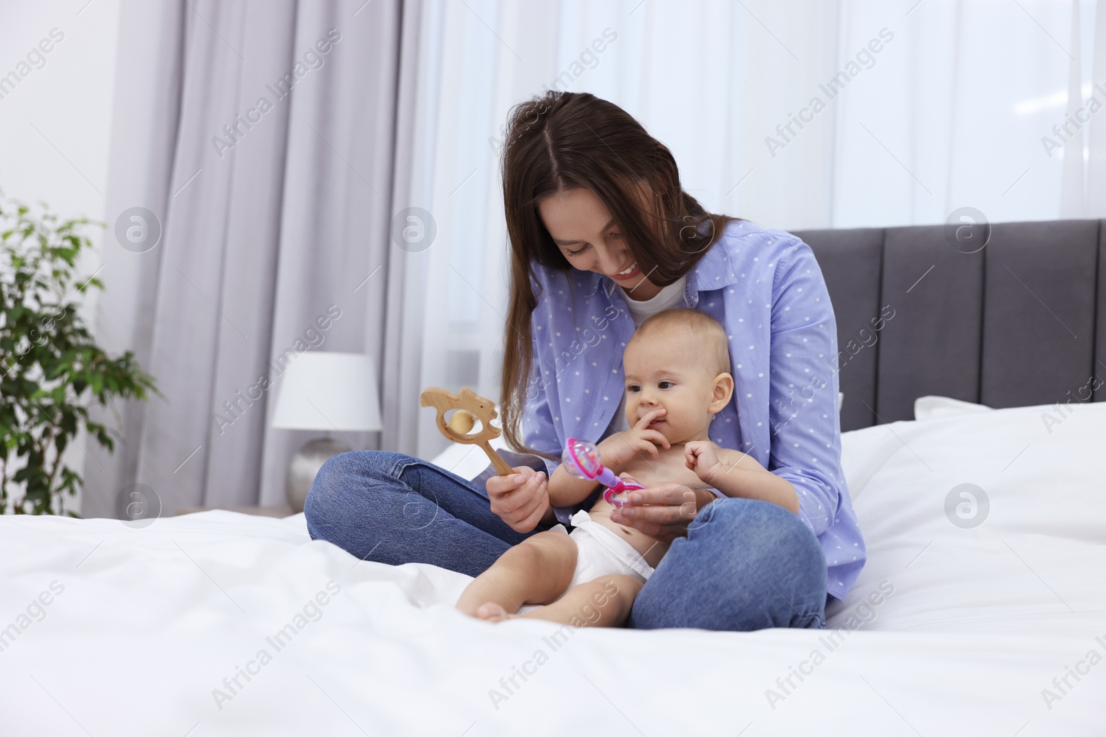 Photo of Mother and her cute little baby with rattles on bed indoors