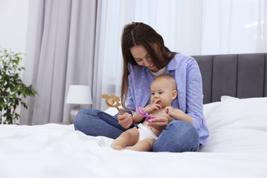 Photo of Mother and her cute little baby with rattles on bed indoors