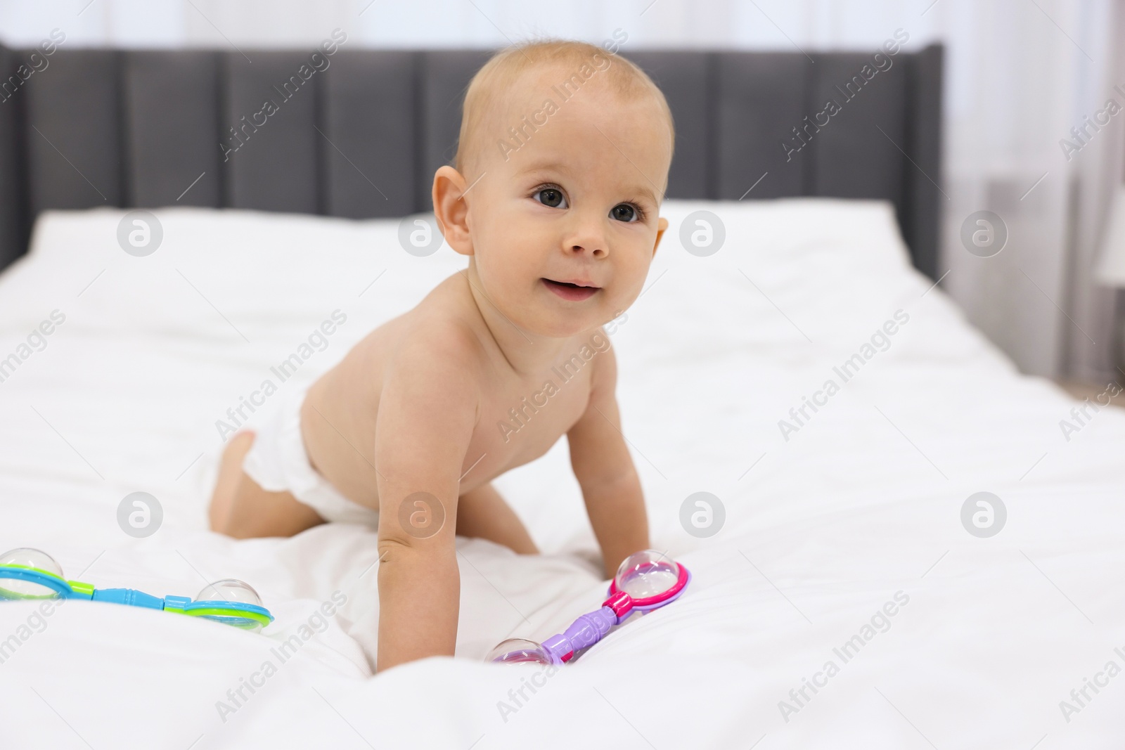 Photo of Cute little baby with rattles on bed indoors, space for text