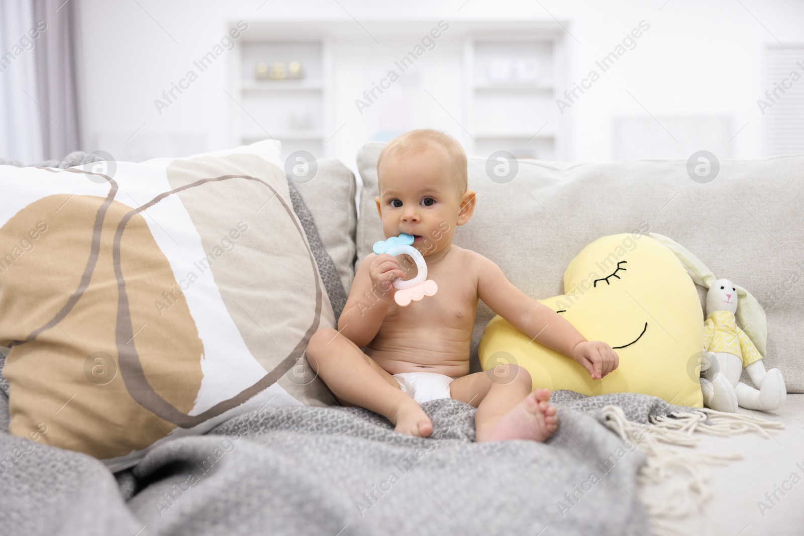 Photo of Cute little baby with rattle on sofa indoors