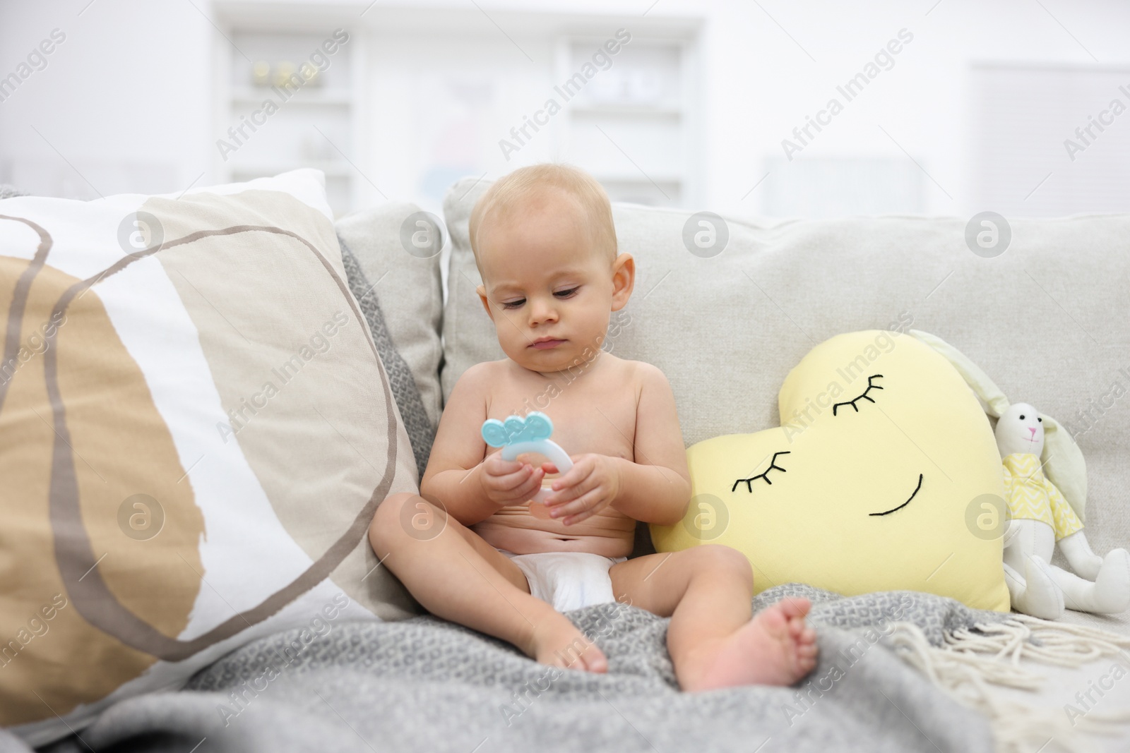 Photo of Cute little baby with rattle on sofa indoors