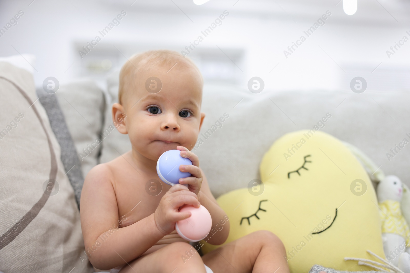 Photo of Cute little baby with rattle on sofa indoors, space for text