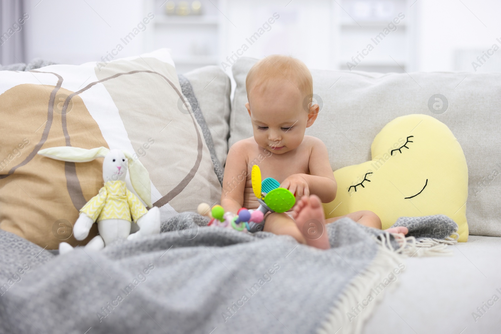 Photo of Cute little baby with rattle and other toys on sofa indoors