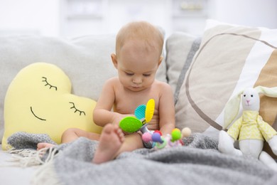 Photo of Cute little baby with rattle and other toys on sofa indoors