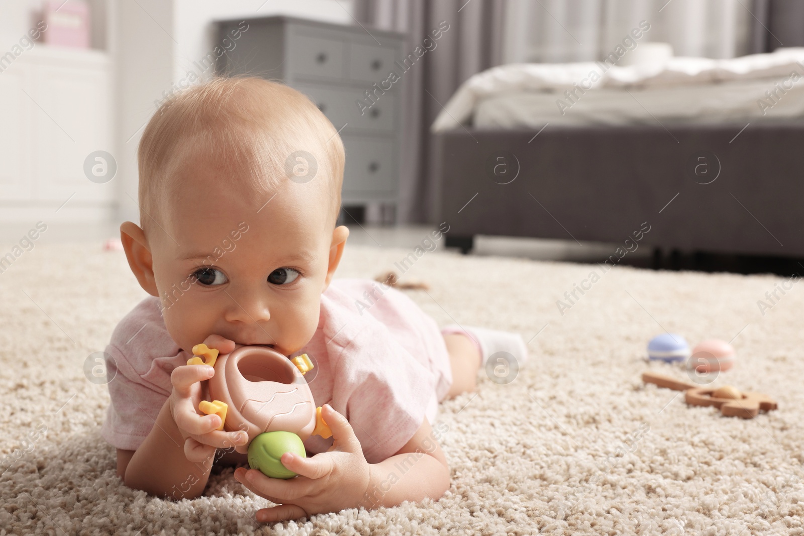 Photo of Cute little baby with rattles on floor indoors, space for text