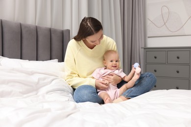 Photo of Mother and her cute little baby with rattle on bed indoors