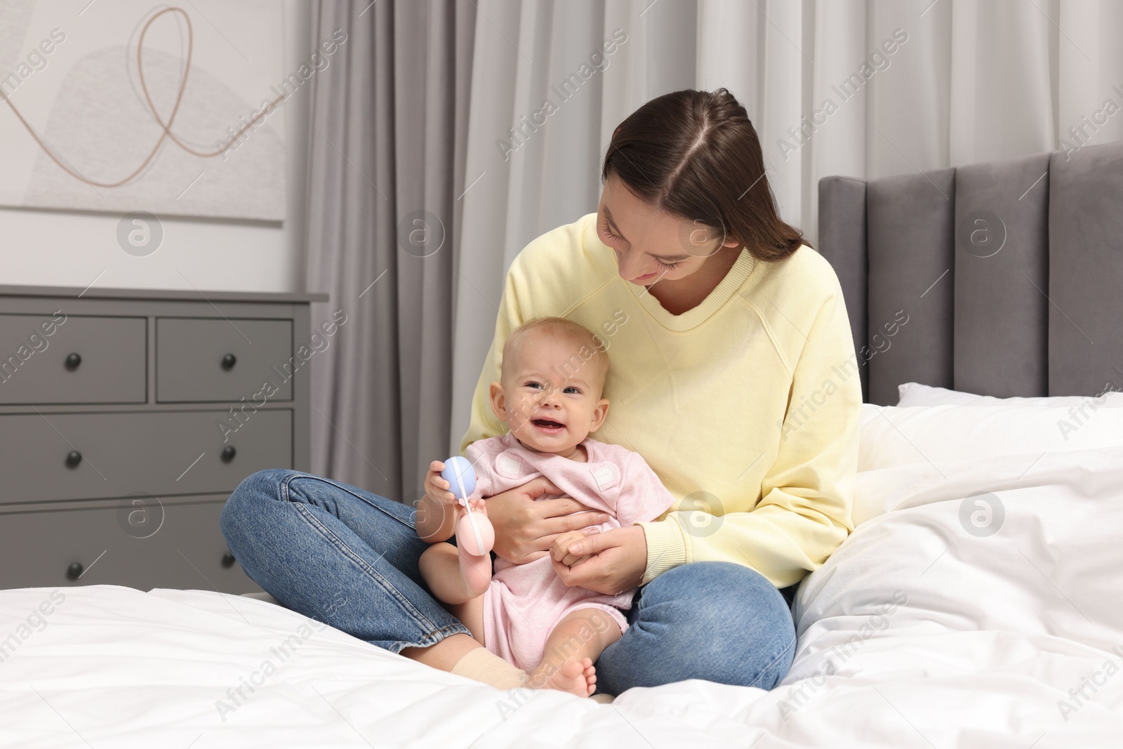 Photo of Mother and her cute little baby with rattle on bed indoors