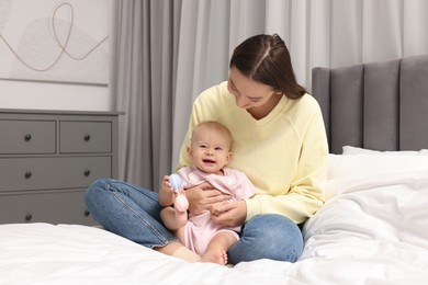 Photo of Mother and her cute little baby with rattle on bed indoors