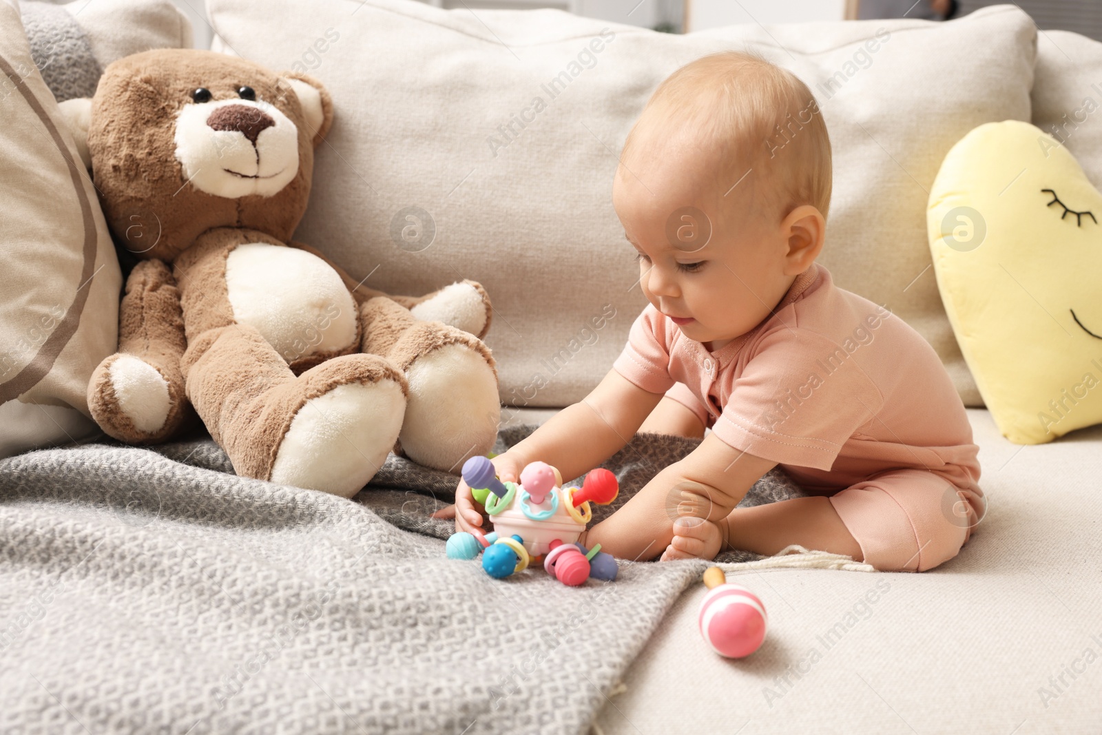 Photo of Cute little baby with rattles and teddy bear on sofa indoors