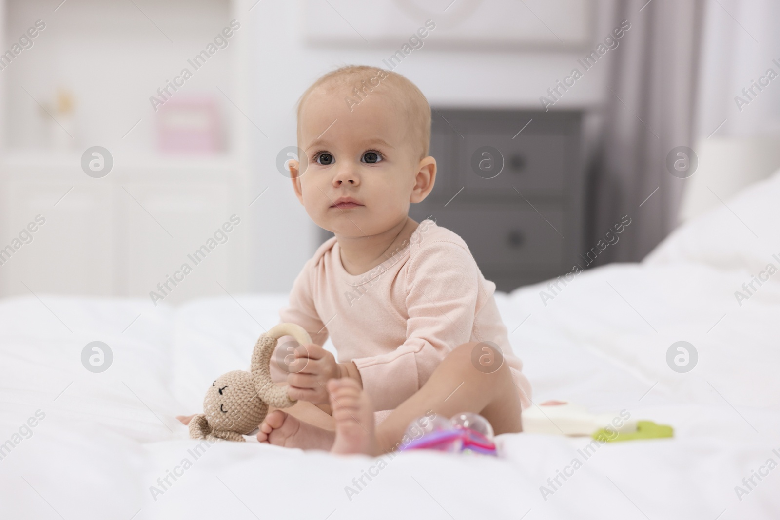 Photo of Cute little baby with rattles on bed indoors