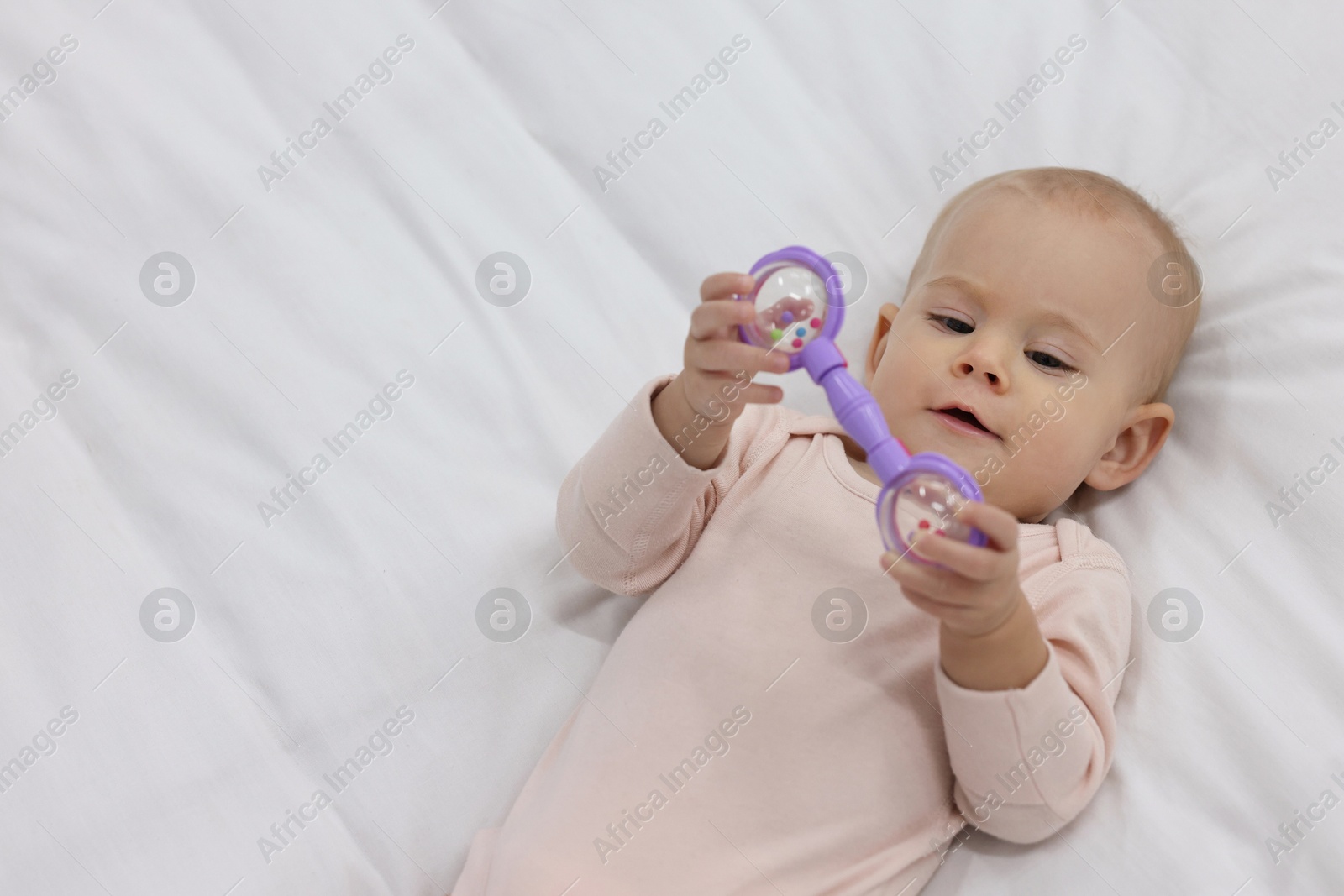 Photo of Cute little baby with rattle on bed indoors, above view. Space for text