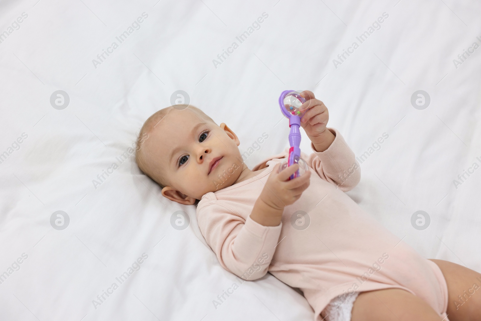 Photo of Cute little baby with rattle on bed indoors