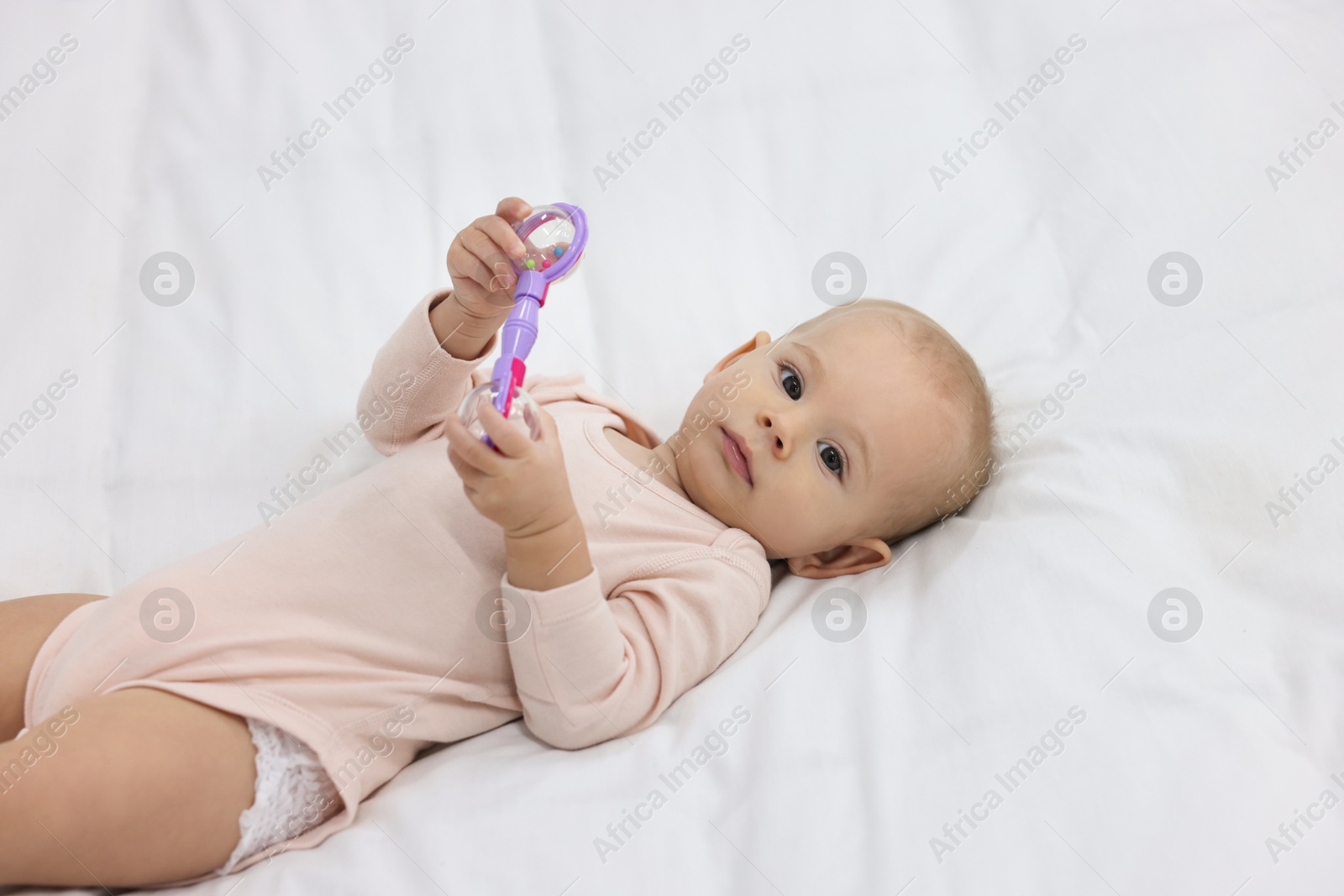 Photo of Cute little baby with rattle on bed indoors