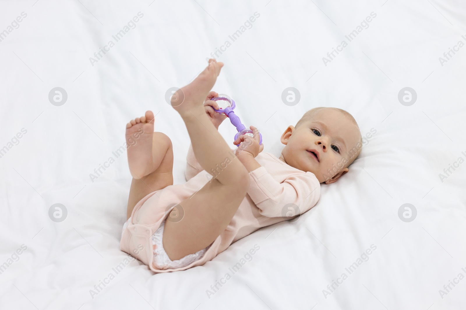 Photo of Cute little baby with rattle on bed indoors