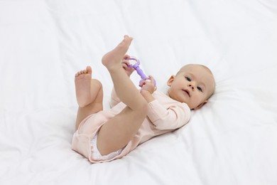 Photo of Cute little baby with rattle on bed indoors