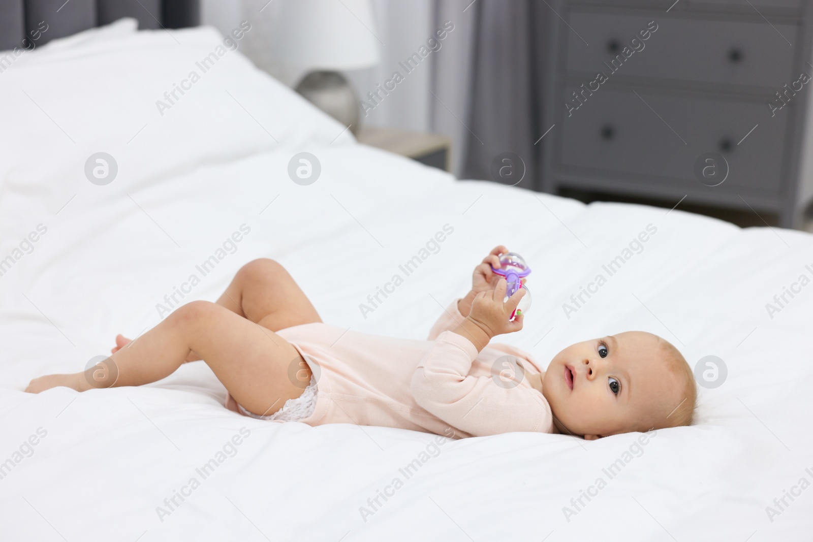 Photo of Cute little baby with rattle on bed indoors