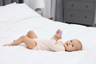 Photo of Cute little baby with rattle on bed indoors