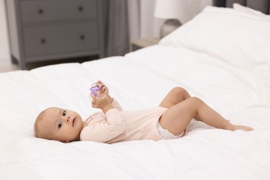 Photo of Cute little baby with rattle on bed indoors