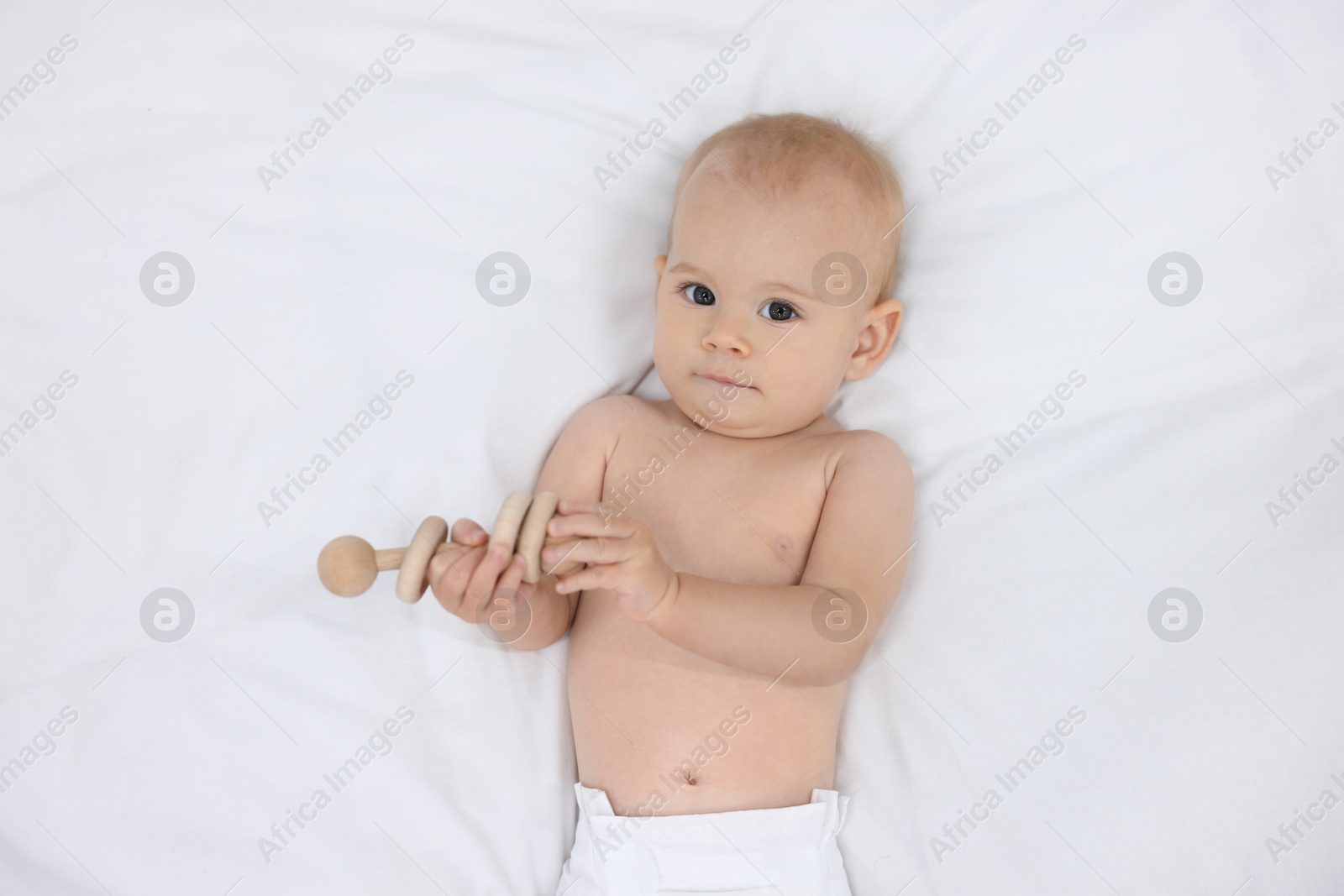 Photo of Cute little baby with rattle on bed indoors, top view