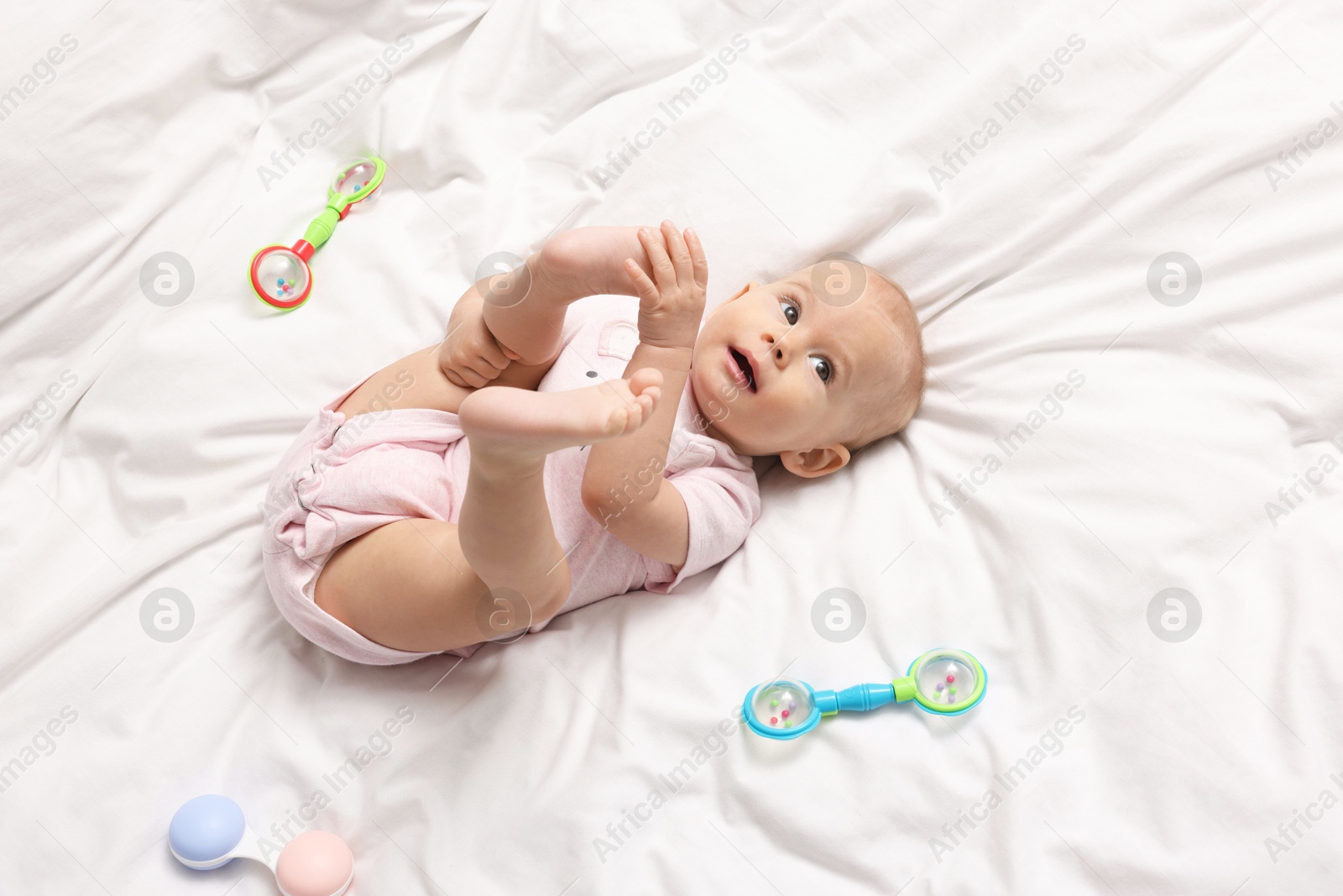 Photo of Cute little baby with rattles on bed indoors, above view