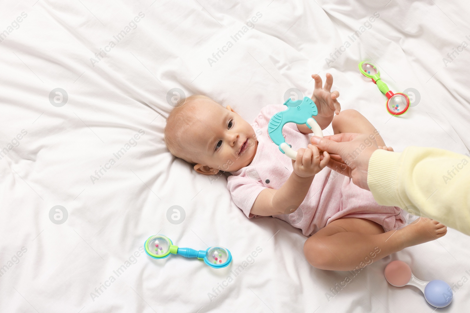 Photo of Mother and her cute little baby with rattle on bed indoors, above view. Space for text