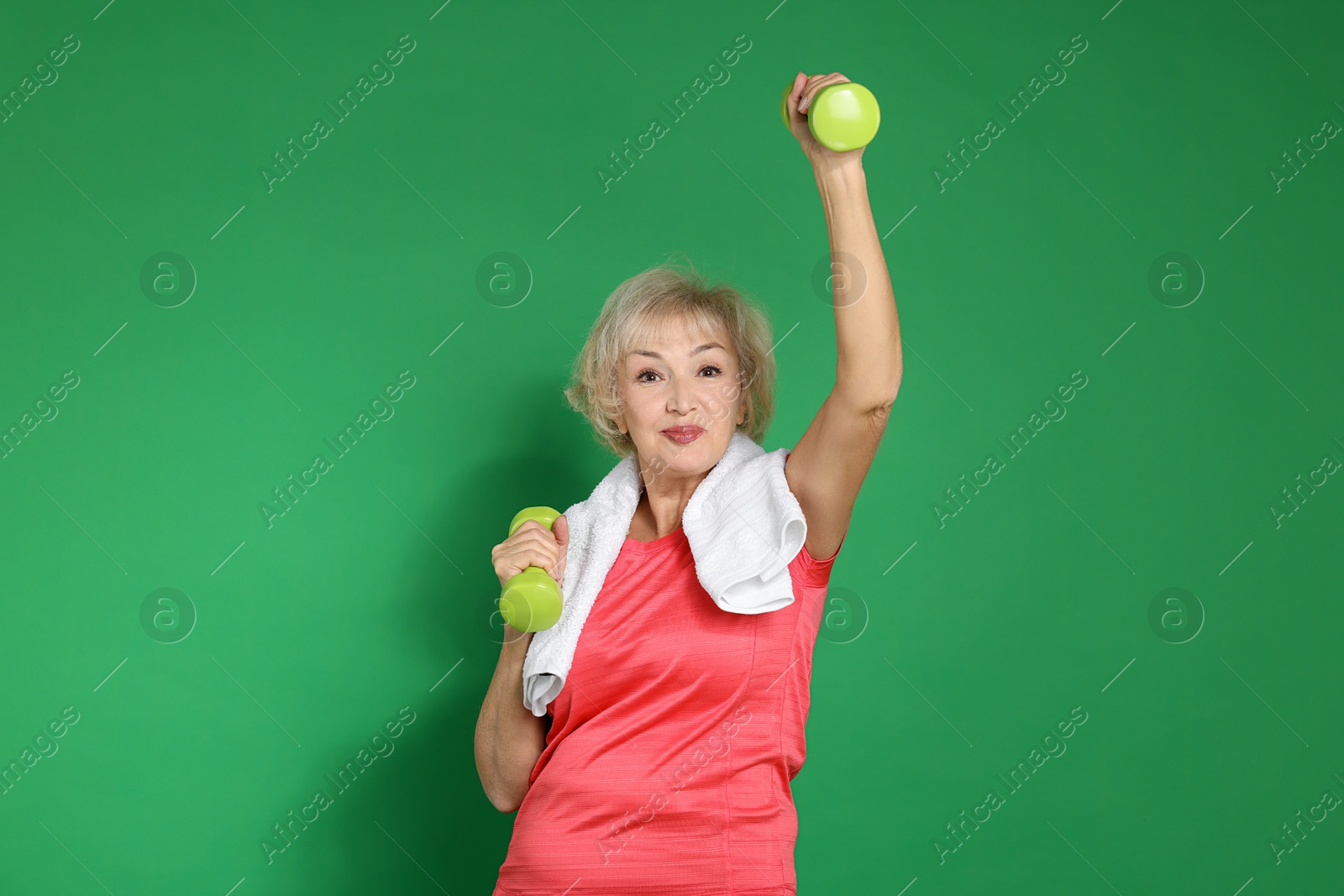 Photo of Senior woman exercising with dumbbells and towel on green background