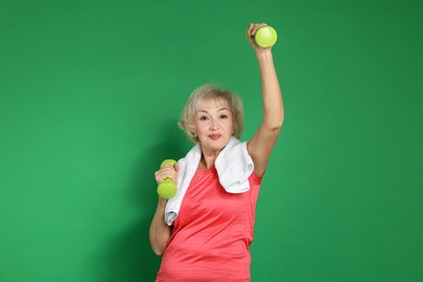 Photo of Senior woman exercising with dumbbells and towel on green background