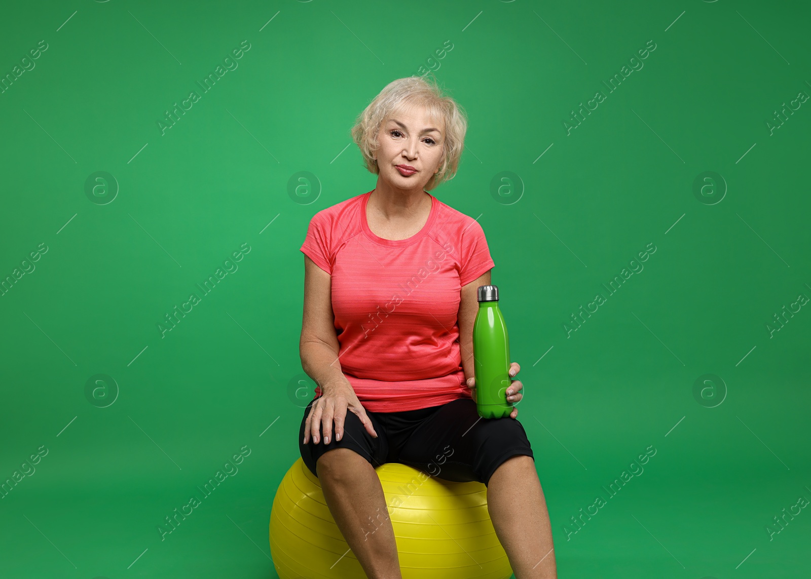 Photo of Senior woman with fitness ball and water on green background, space for text