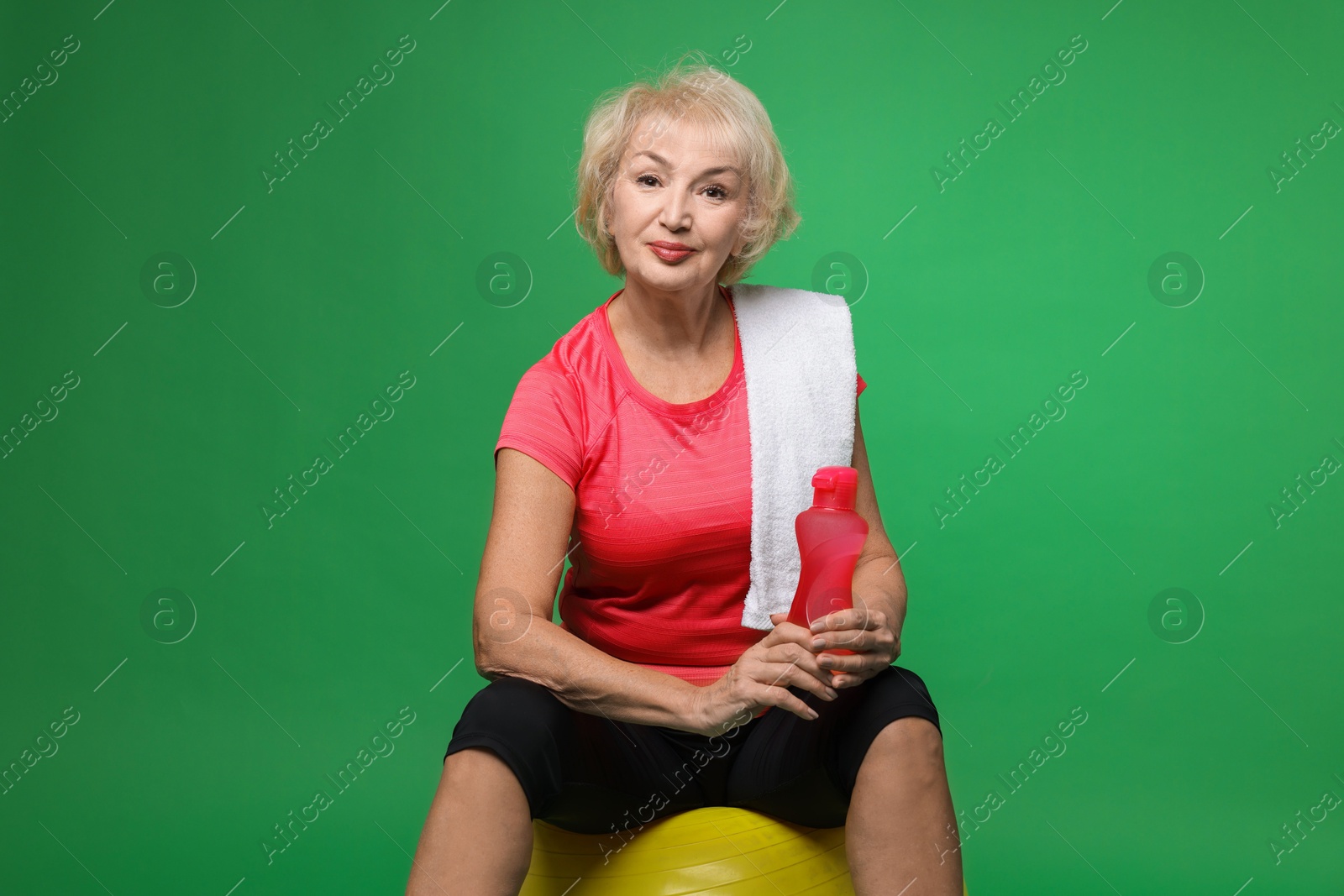 Photo of Senior woman with fitness ball, water and towel on green background