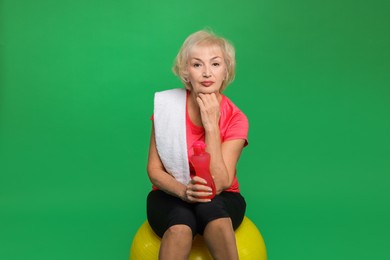 Photo of Senior woman with fitness ball, water and towel on green background