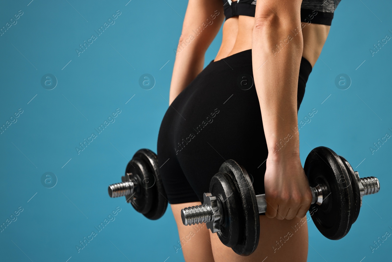 Photo of Woman in gym clothes exercising with barbells on light blue background, closeup. Space for text