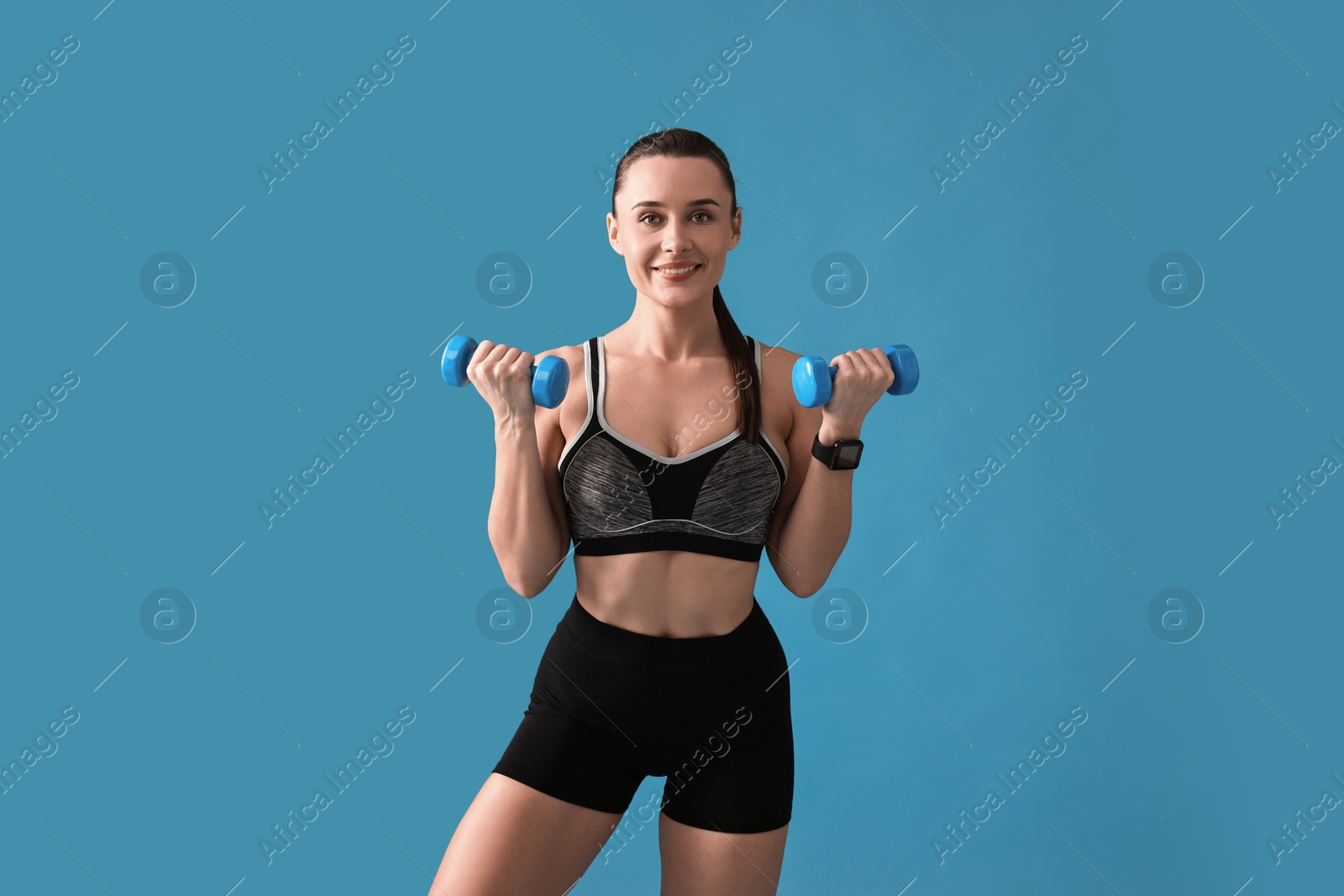 Photo of Woman in gym clothes exercising with dumbbells on light blue background