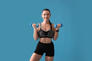 Photo of Woman in gym clothes exercising with dumbbells on light blue background