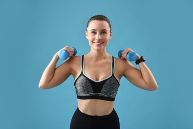 Photo of Woman in gym clothes exercising with dumbbells on light blue background